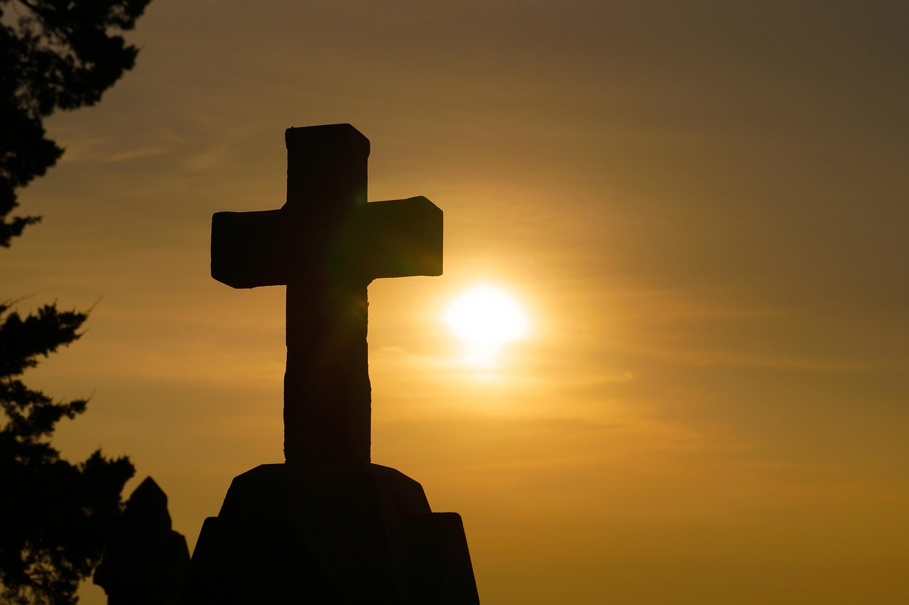 A wooden cross silhouetted against a dramatic sky